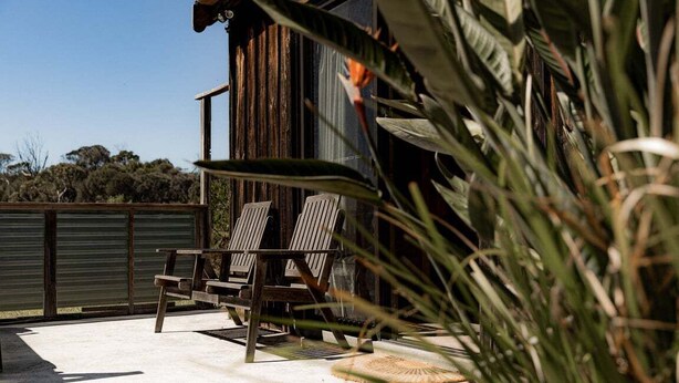 A patio with two wooden chairs and a table, surrounded by lush greenery. - Geoff's ~ beach, bush and bliss (Break O'Day)
