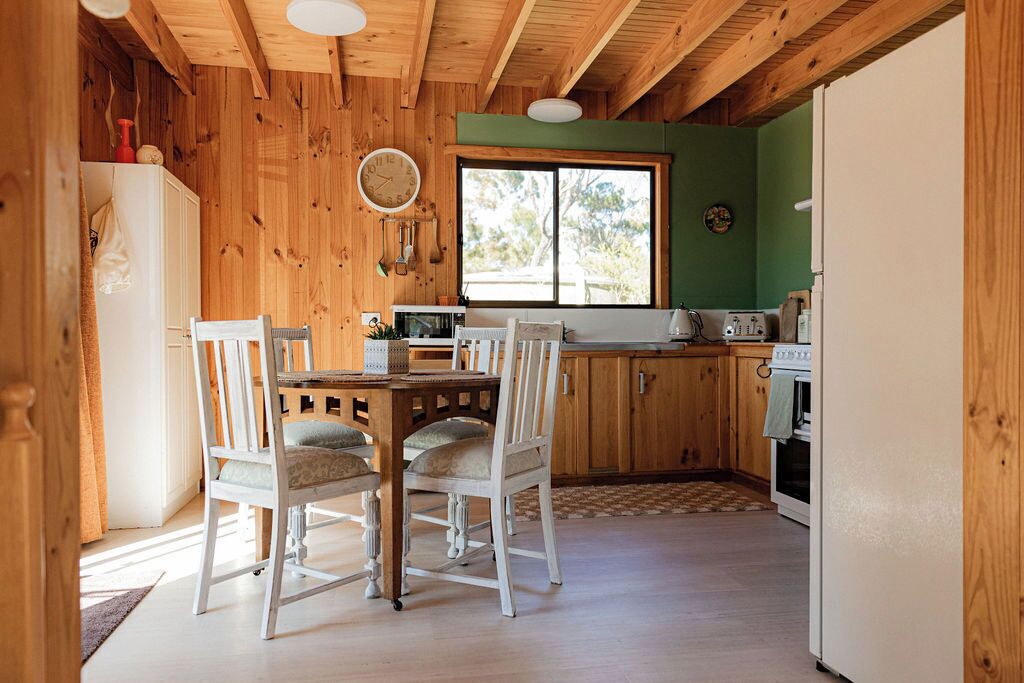 Un intérieur en bois comprenant une table et des chaises, une cuisine avec des meubles en bois, un réfrigérateur et une fenêtre.