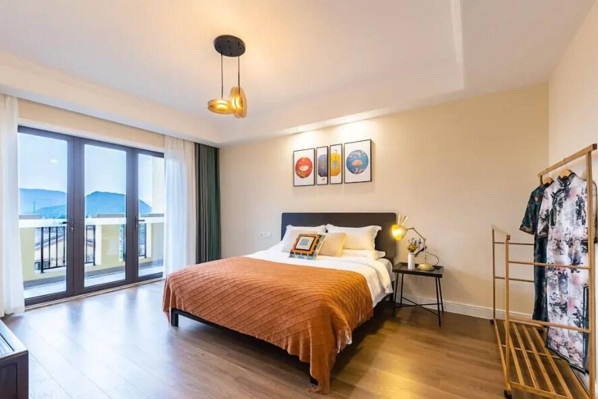 Une chambre d’hôtel avec un lit, une table de chevet, une lampe, un étendoir et une grande fenêtre donnant sur un beau paysage.
