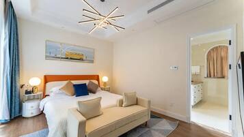 A modern hotel room with a large bed, bedside tables with lamps, a sofa, a ceiling light fixture, and a door leading to a bathroom.