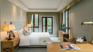 Een hotelkamer met een bed, nachtkastjes, een bureau en uitzicht op groen.