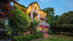 Een tweelaags huis met een balkon, omringd door weelderige begroeiing en een verzorgd gazon.