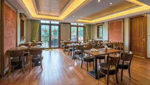 Een ruime eetruimte met meerdere tafels en stoelen, grote ramen met uitzicht op de omgeving, en een houten plafond met inbouwverlichting.