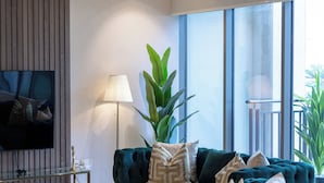 A modern living room with a dark green sofa, a large potted plant, and a flat-screen TV mounted on the wall. - Durrani Homes - The Luxe Retreat 4BR Podium villa with private Jacuzzi and Burj Khalifa View (Dubai)