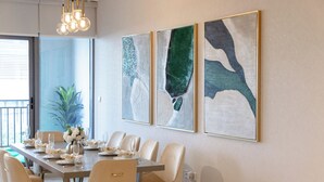 A dining area with a long table set for six, surrounded by six chairs. There are three framed abstract paintings on the wall above the table. - Durrani Homes - The Luxe Retreat 4BR Podium villa with private Jacuzzi and Burj Khalifa View (Dubai)