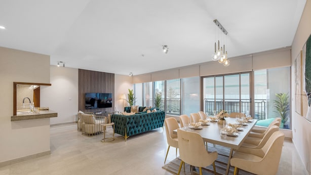 A spacious living area with a dining table set for six, a teal sofa, and a television. - Durrani Homes - The Luxe Retreat 4BR Podium villa with private Jacuzzi and Burj Khalifa View (Dubai)