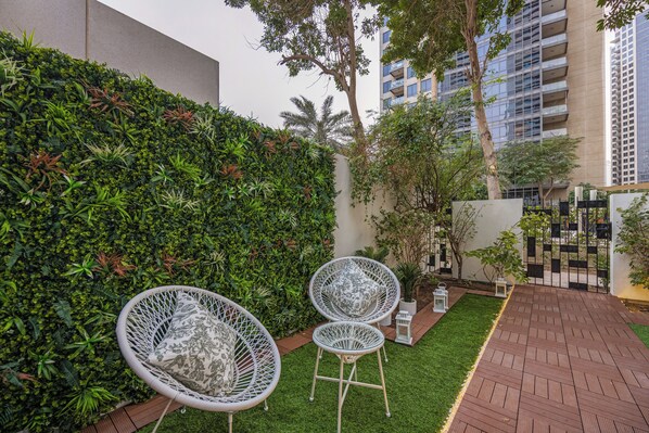 A courtyard with two white wicker chairs, a small table, and a neatly trimmed hedge.