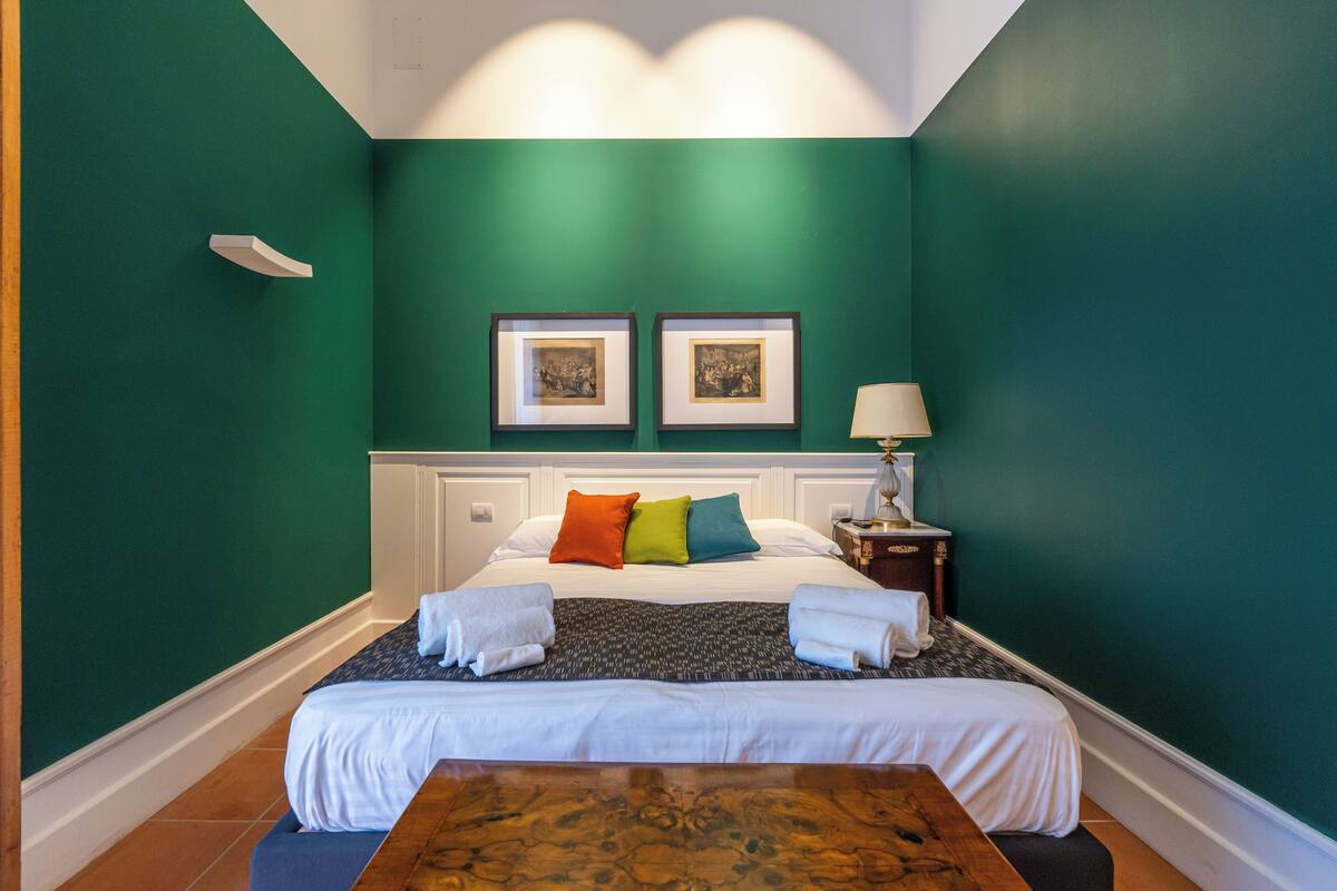 A hotel room with a large bed, a bedside table with a lamp, and two framed pictures on the wall.
