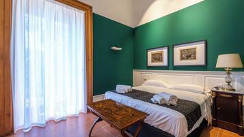 A hotel room with a bed, a table, a lamp, and two framed pictures on the wall.