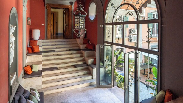 A grand staircase leading to an upper floor, with a large arched window offering a view of the street below. - CORTE SATRIANO RESIDENCE (Naples)