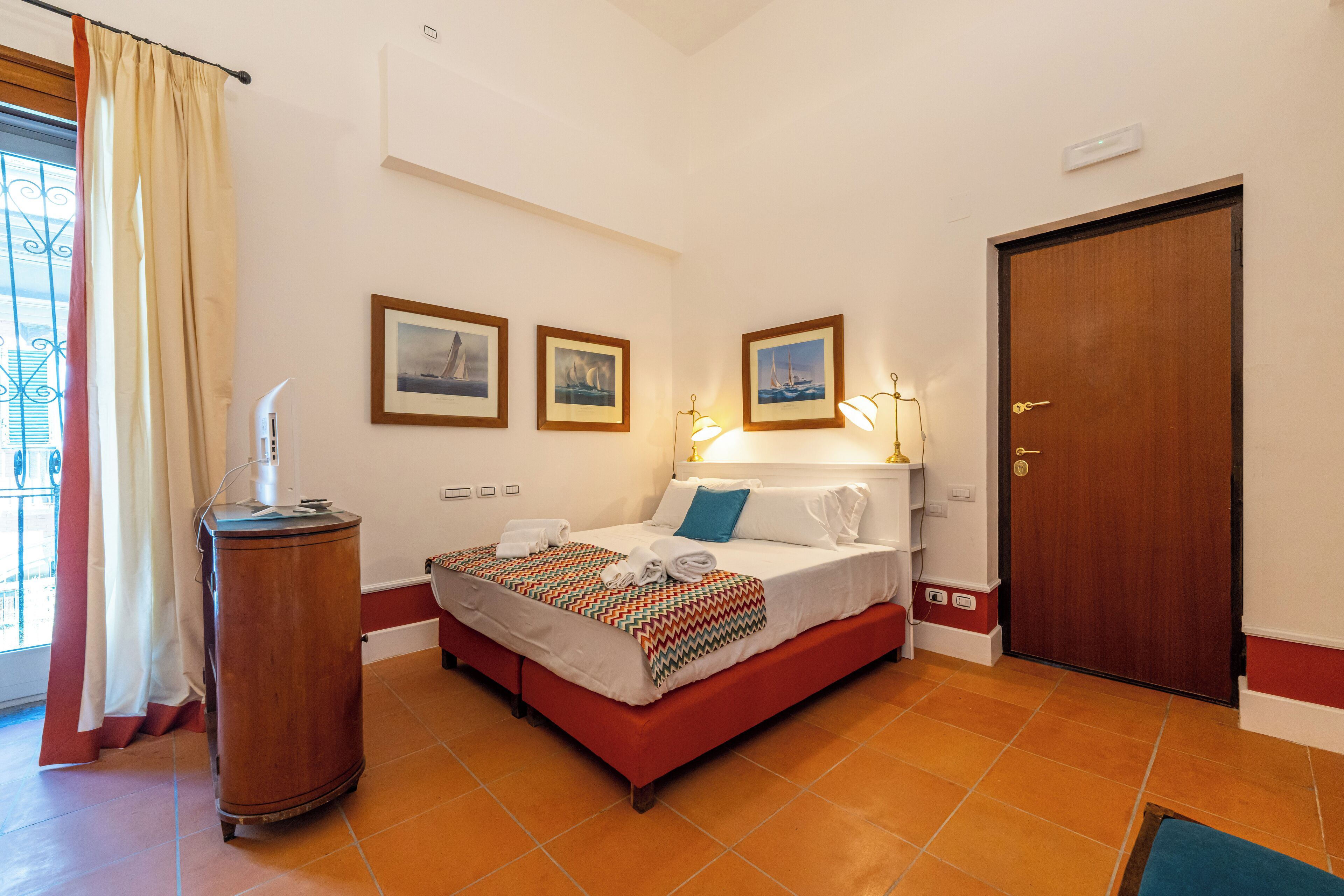 A hotel room with a bed, a bedside table, a wardrobe, and a window with curtains.