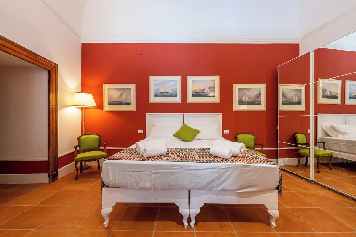 A hotel room with a large bed, a mirror, and a red wall with framed pictures.
