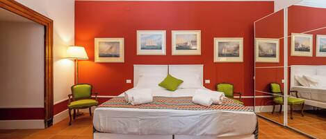 A hotel room with a large bed, a mirror, and a red wall with framed pictures.