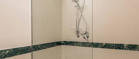 A modern bathroom with a glass-enclosed shower, a sink, and marble-tiled walls.