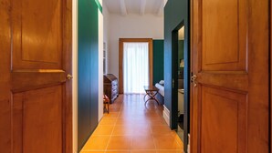 A hallway with wooden doors, a tiled floor, a bed, a dresser, and a window with curtains. - CORTE SATRIANO RESIDENCE (Naples)