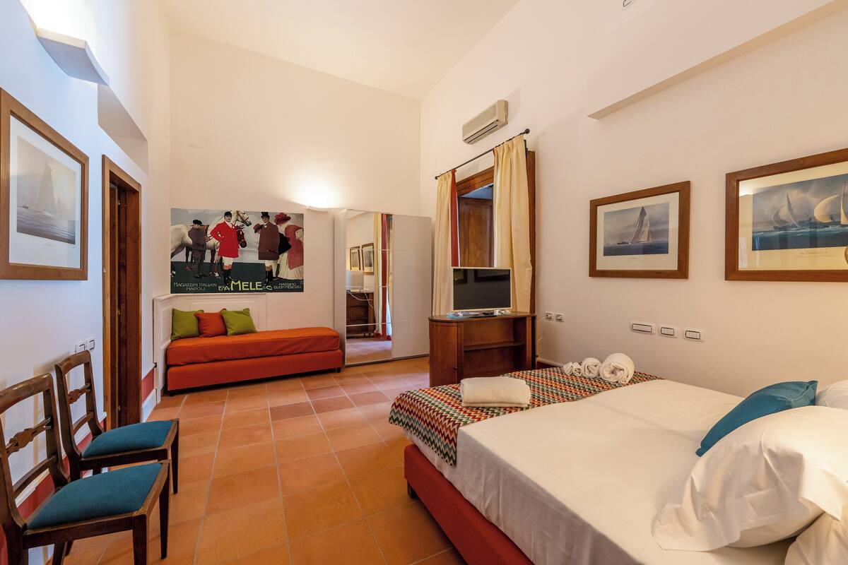 A hotel room with a bed, a sofa, a TV, and a poster on the wall.