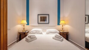 A hotel room with a large bed, two bedside tables with lamps, a framed picture on the wall, and a mirror on the right wall. - CORTE SATRIANO RESIDENCE (Naples)