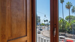 A view from a window with wooden frames, looking out onto a busy street with cars and palm trees. - CORTE SATRIANO RESIDENCE (Naples)