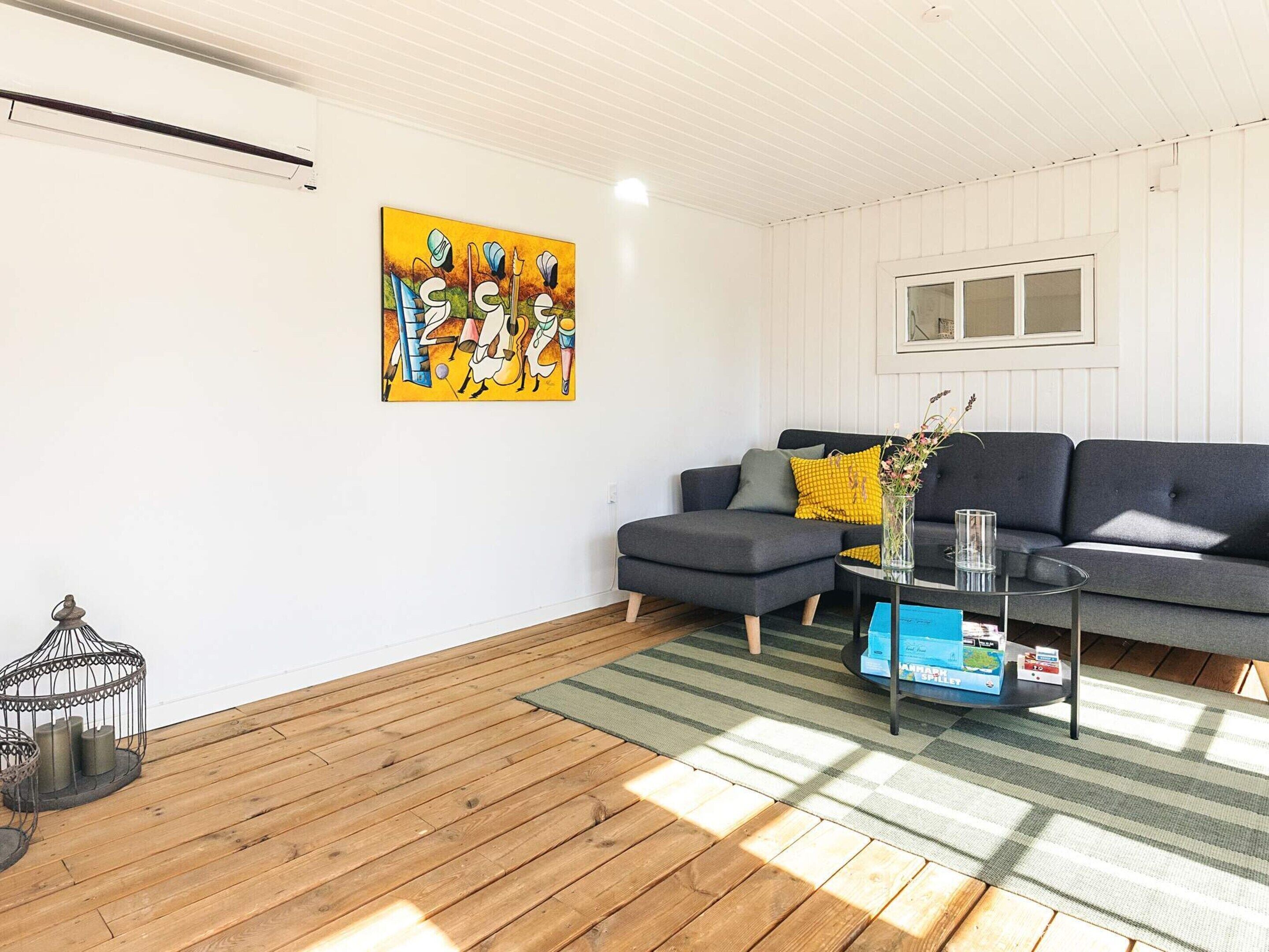 A living room with a grey sectional sofa, a glass coffee table, and a colorful abstract painting on the wall.