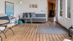 Un salon chaleureux avec un canapé gris, une petite table et un fauteuil en osier. Une carte est accrochée au mur et le plafond est en bois.