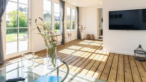 Une pièce spacieuse avec de grandes fenêtres, une table ronde en verre et un téléviseur à écran plat fixé au mur.