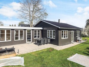 Una casa moderna de dos pisos con ventanas amplias, un patio con mobiliario exterior y un césped bien cuidado.
