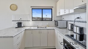 Uma cozinha moderna com armários brancos, forno embutido, micro-ondas, torradeira e janela com vista para edifícios.