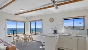 Uma cozinha moderna com vista para o oceano, uma área de jantar com mesa e cadeiras, e um ventilador de teto.