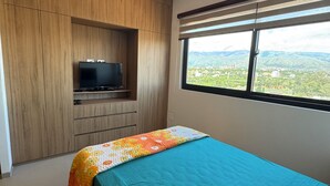 A bedroom with a bed, a TV on a wooden cabinet, and a window with a view of greenery. - Serene studio with Pool and Wifi in charming Tarija (Tarija)
