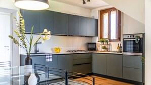Une cuisine moderne avec des meubles gris, un plan de travail noir, une table à manger avec des chaises, un vase de fleurs et une fenêtre donnant sur un beau paysage.