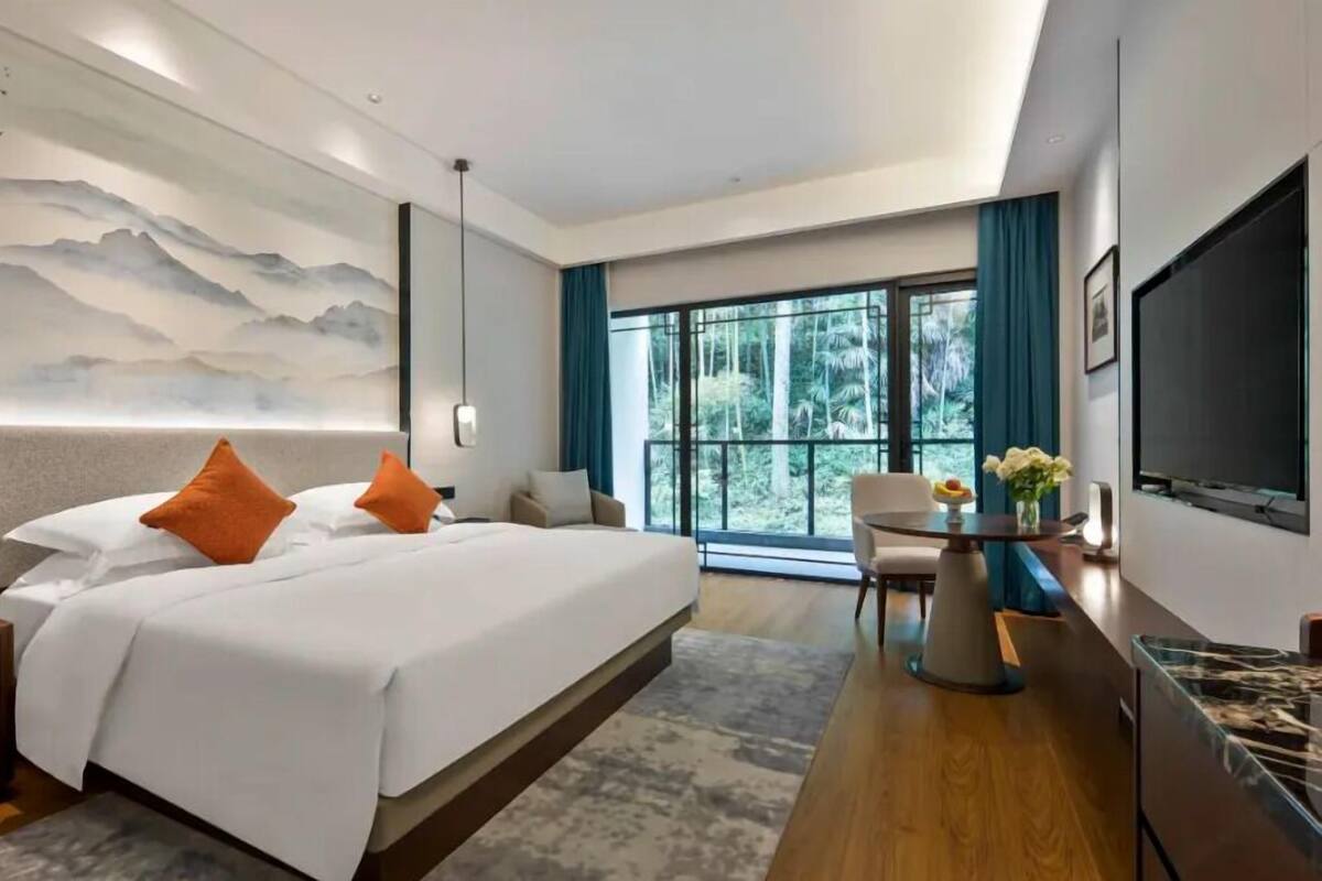 A modern hotel room with a large bed, a desk, a chair, and a TV.