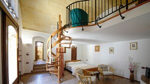 A spacious room with a spiral staircase, a bed, two wicker chairs, and a small table. - Lovely house with AC in Matera - Perfect for a getaway (Matera)