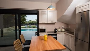 A modern kitchen with white cabinets, a wooden dining table, and a built-in oven. - VILLA PENELOPE
 (Katouna)