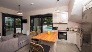 A modern kitchen with a wooden island, white cabinets, and stainless steel appliances. There is a dining area with a sofa and chairs, and a large window offering a view of the outdoors. - VILLA PENELOPE
 (Katouna)