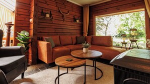 A cozy log cabin interior with a sofa, two round coffee tables, and a large window with a view of greenery. - Spectacular Dune Villa with a private sauna and breathtaking views of the dunes (Soest)