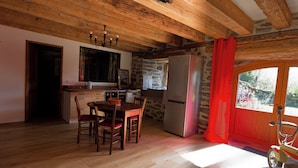 Una cocina rústica con vigas de madera, pared de piedra, refrigerador y una mesa de comedor con sillas.