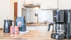 Een keuken met een koffiezetapparaat, een waterkoker en twee blikjes frisdrank op het aanrecht.