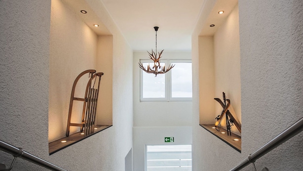 Una escalera moderna con barandillas metálicas, un candelabro y decoración montada en la pared.