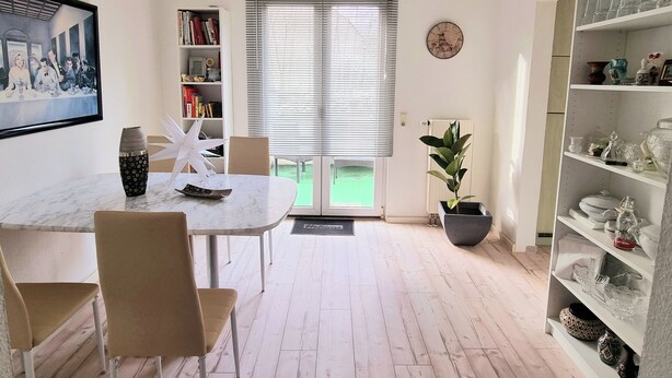 A dining area with a white table and chairs, a bookshelf, a potted plant, and a clock on the wall. - Fully equipped vacation apartment with plenty of space, barbecue and garden, centrally located (Waltershausen)