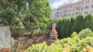 A garden with a brick oven, surrounded by greenery and a building in the background. - Fully equipped vacation apartment with plenty of space, barbecue and garden, centrally located (Waltershausen)