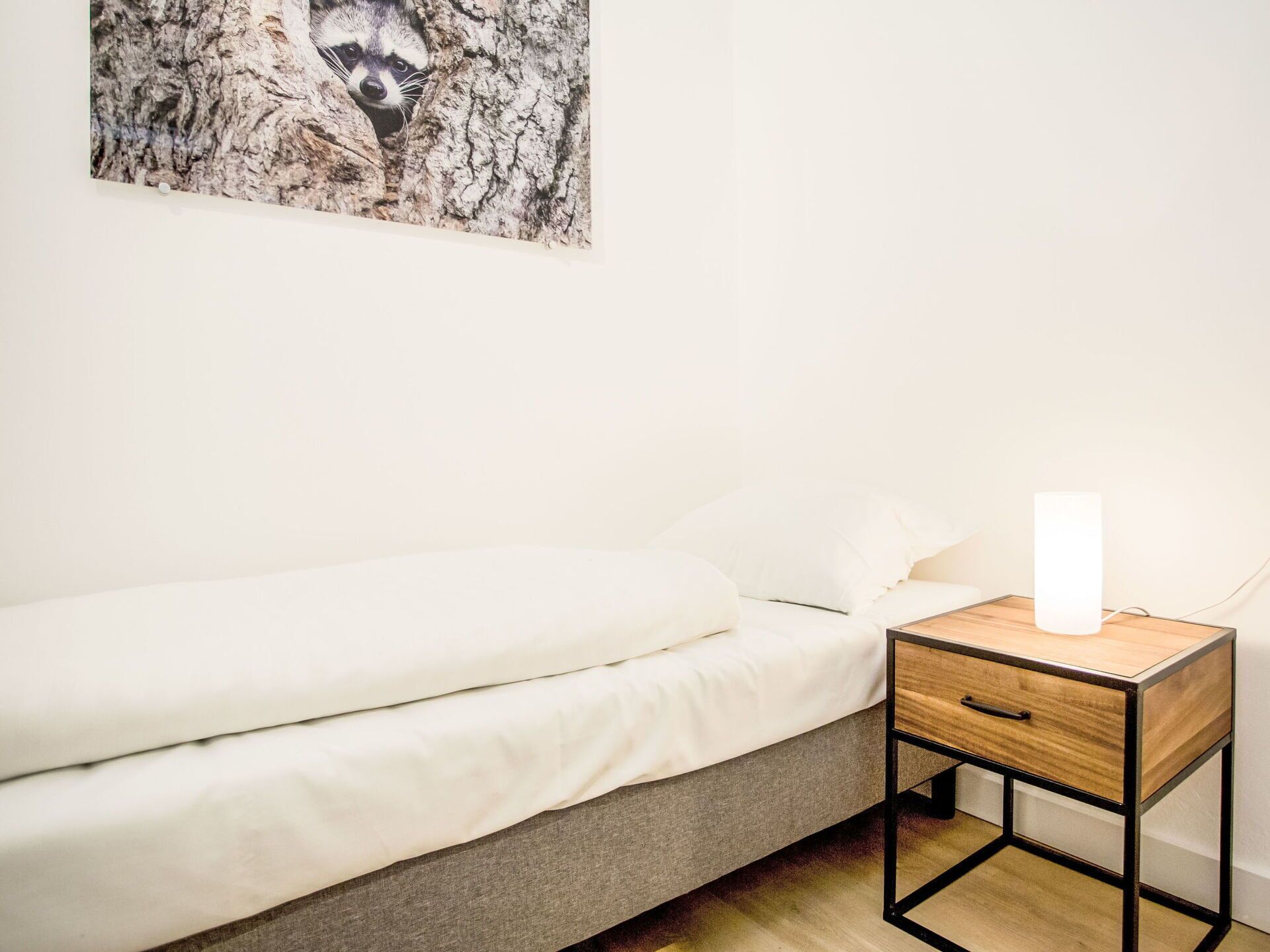 A minimalist bedroom with a bed, a bedside table, and a wall-mounted picture.