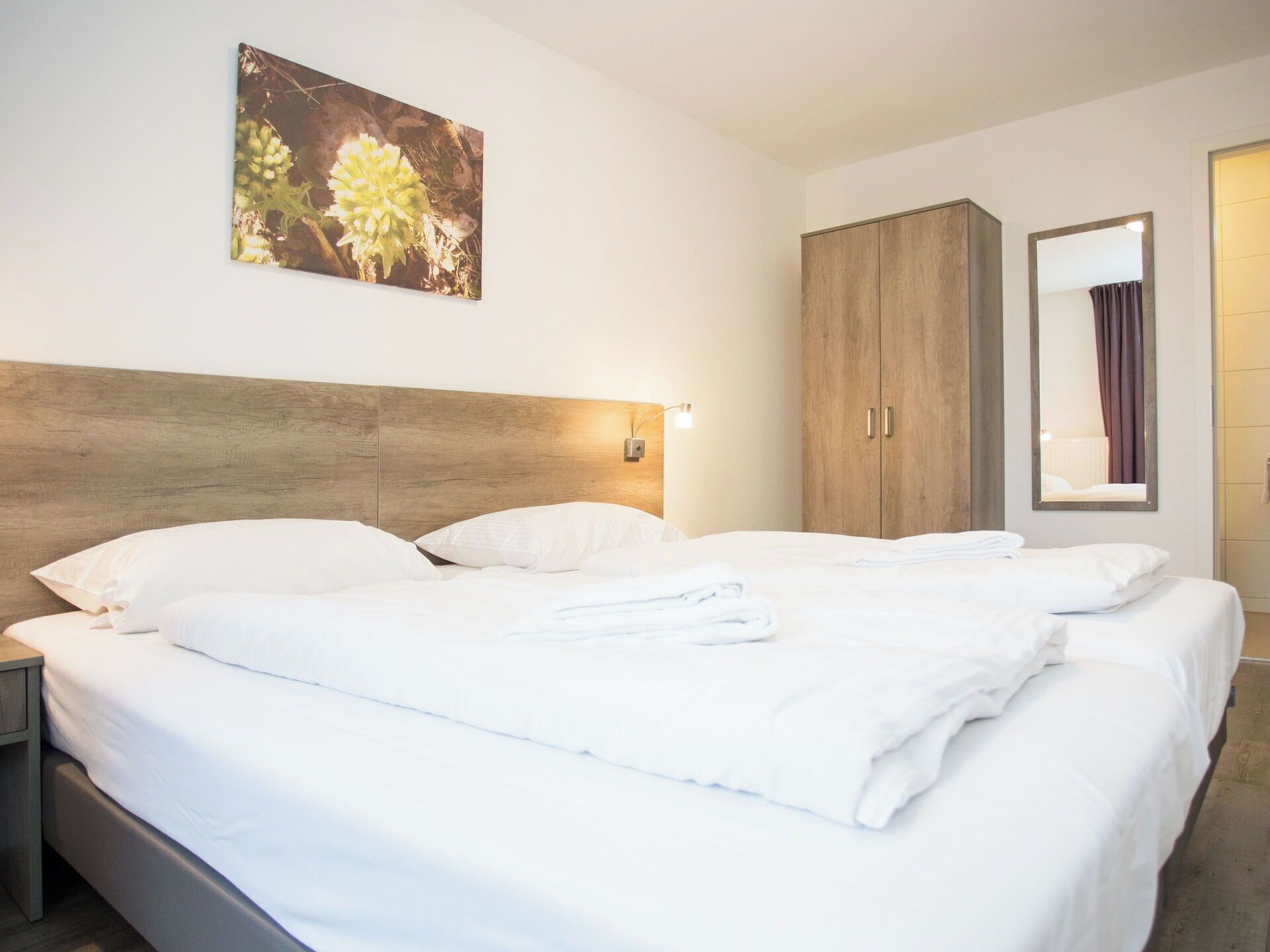 Habitació d'hotel amb un llit gran, un panell de capçalera de fusta, una tauleta de nit, un armari i un mirall.