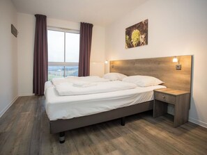 Ein Hotelzimmer mit einem großen Bett, einem Nachttisch, einer Wandlampe und einem Fenster mit Vorhängen.