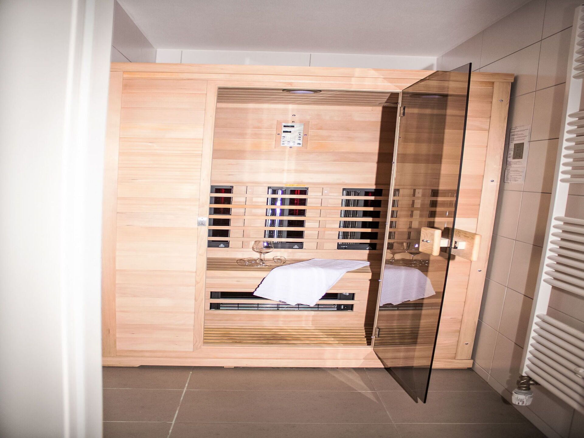 Et moderne sauna miljø med træpaneler, en glasdør og en bænk.