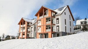 Un hotel de varios pisos con balcones, una pista de esquí en primer plano y cielo despejado.