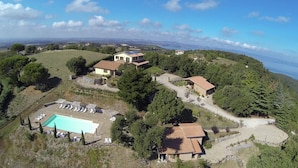 An aerial view of a property with a swimming pool, multiple buildings, and surrounding greenery.