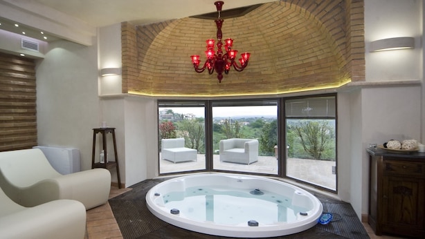 A modern spa room with a glass hot tub, white sofas, and a large window offering a view of the outdoors.