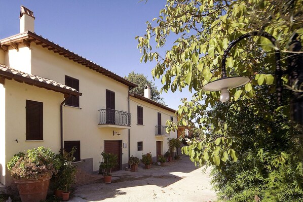 A building with a tiled roof, multiple windows, and a small balcony. There are potted plants in front of the building. - Farmhouse in Lazio with Lake Bolsena Views (Montefiascone)