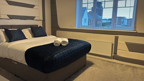 Un dormitorio moderno con una cama grande, vistas de la ciudad a través de la ventana y un radiador en la pared.