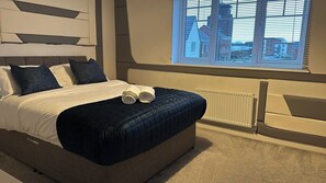 Een moderne slaapkamer met een groot bed, uitzicht op de stad door het raam en een radiator aan de muur.
